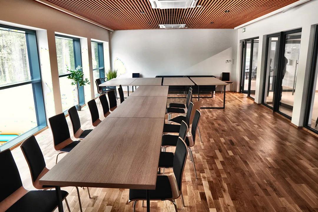 Sala konferencyjna z długim stołem i widokiem na las przez przeszkloną ścianę